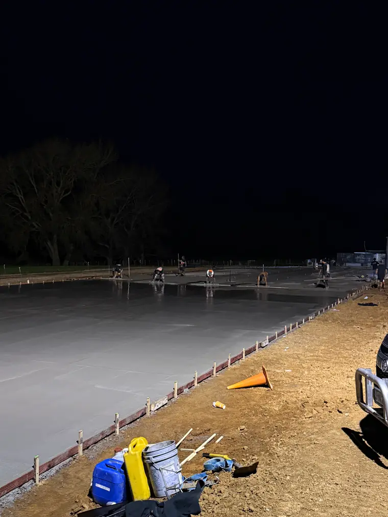 Large slab freshly poured at night with the finishing gear stacked at the edge