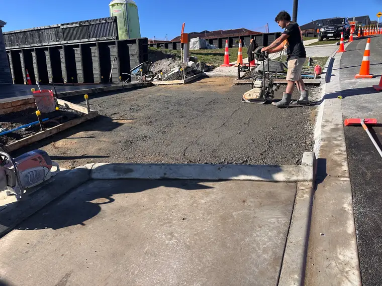 Plate compactor being run over the base of a new footpath, traffic cones set out on the road