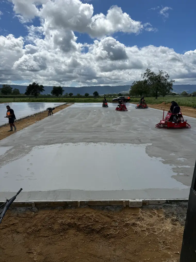 Power trowels finishing the far end of a large farm slab under a big Waikato sky