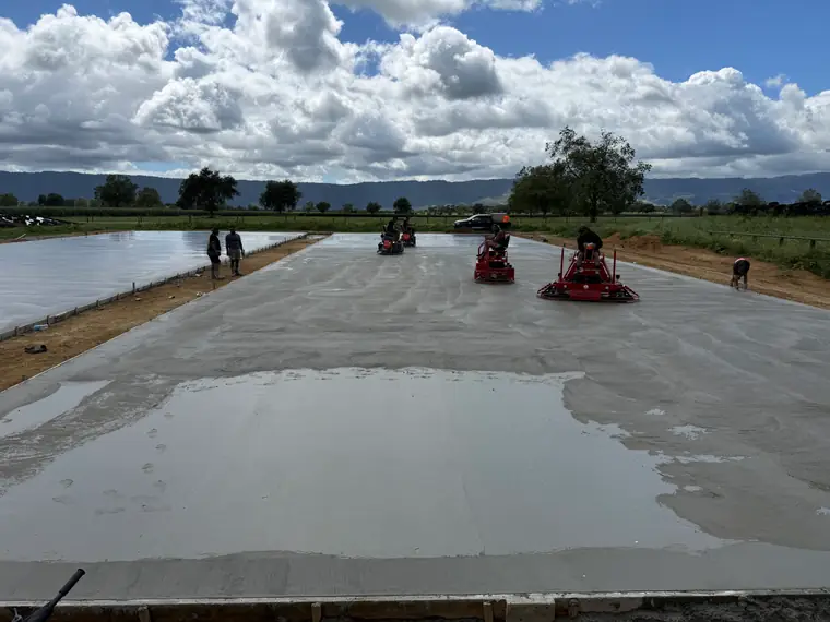 Ride-on power trowels working a large freshly floated concrete slab in open farmland