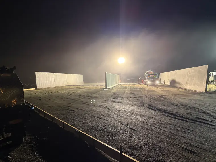 Precast concrete panel walls standing in the dust and floodlight during a night shift