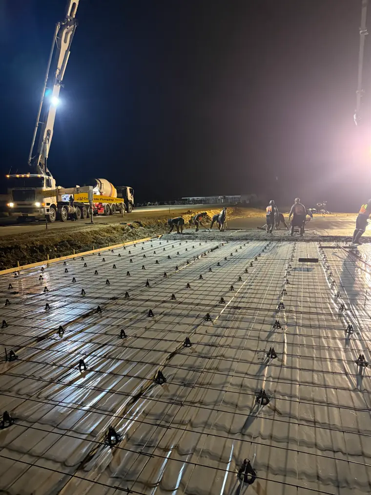 Reinforcing steel and chairs set out along a long slab, floodlit ready for a night pour