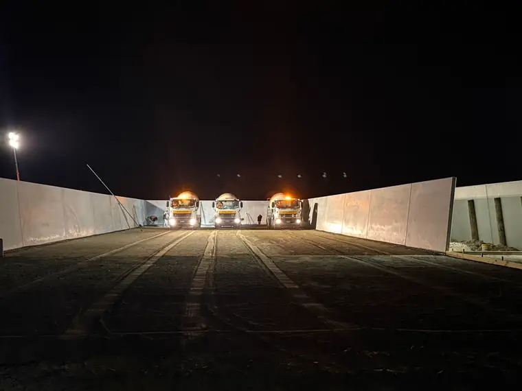 Three ready-mix trucks lined up between the precast walls of a silage bunker before the pour
